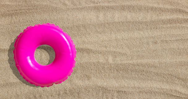 Roze opblaasbare zwembadring op zand - Foto, afbeelding