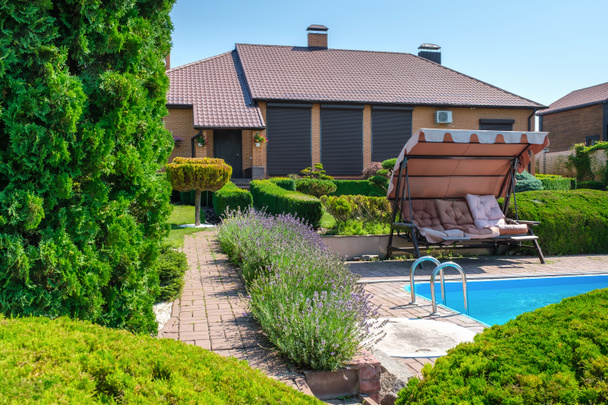 Вилла в европейском стиле с бассейном и садом с красиво отделанными кустами и камнями перед домом. Пейзаж дизайн. Высокое качество фото - Фото, изображение