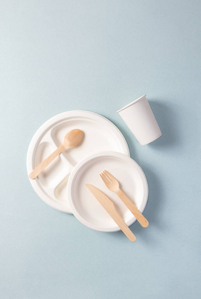 Plastic-free disposable tableware, vertical. Paper plate, food containers, glass, wooden spoon, fork, knife. Single-use dinnerware non-plastic - Photo, Image