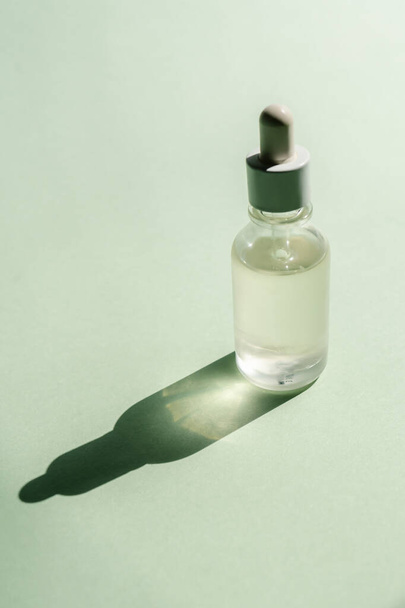 A bottle of serum stands on a green background. - 写真・画像