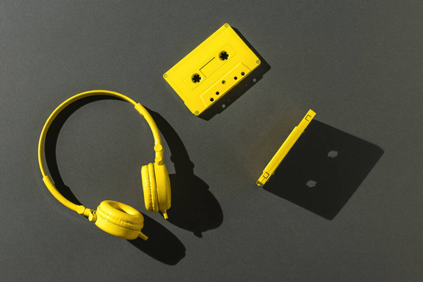 Due cassette con nastro magnetico e cuffie gialle in luce intensa su sfondo grigio. Tendenza colore. Attrezzature vintage per ascoltare musica. Posa piatta. - Foto, immagini