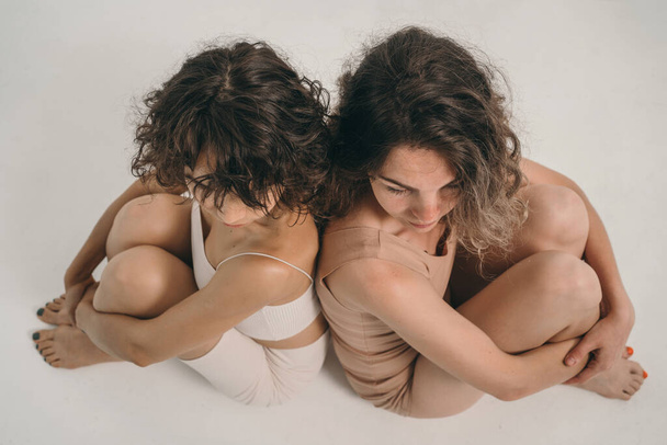 A beautiful girl with curly hair looks into the frame. A girl without makeup. A beautiful and natural woman. Minimalism in appearance. Two girls in their underwear are sitting next to each other. - Photo, Image