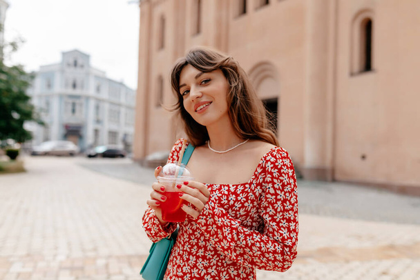 Outside portrait of attractive stylish girl in colorful summer dress holding summer drink and waling in summer city. High quality photo - Photo, Image