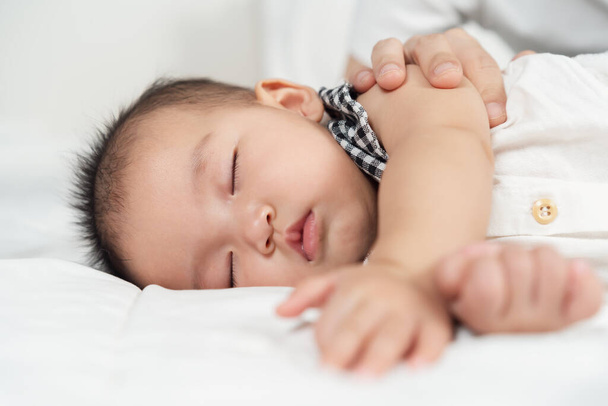 baby sleeping on a bed with hand patting - 写真・画像