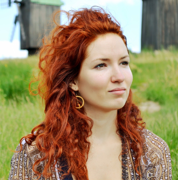 mooie jonge redhead vrouw weg op zoek en denken op de achtergrond van de molens - Foto, afbeelding