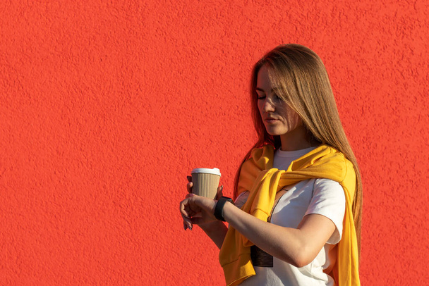 Ritratto esterno di giovane donna con caffè mattutino in mano. La donna sta guardando l'orologio. - Foto, immagini
