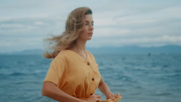 A slim blonde in a yellow dress walks along the beach and looks around - Séquence, vidéo