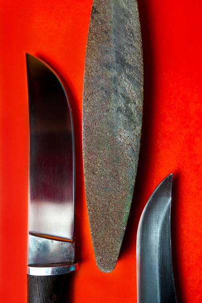 dos cuchillos hechos a mano y una barra para afilar sobre un fondo rojo - Foto, imagen