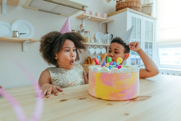 Счастливая девушка смотрит на именинный торт со свечами, весело проводя время во время празднования дня рождения на кухне. Выборочный фокус на лице девушки. - Фото, изображение