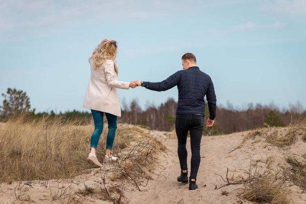 Egy fiatal pár sétáló homokdűnék fogták egymás kezét.A távolban, az erdőben.Kaland utazás életmód koncepció. - Fotó, kép