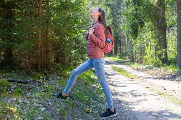 Hübsches junges Touristenmädchen entspannt sich auf der Waldstraße. Teenager mit Rucksack im grünen Wald Sommer oder Frühling. - Foto, Bild