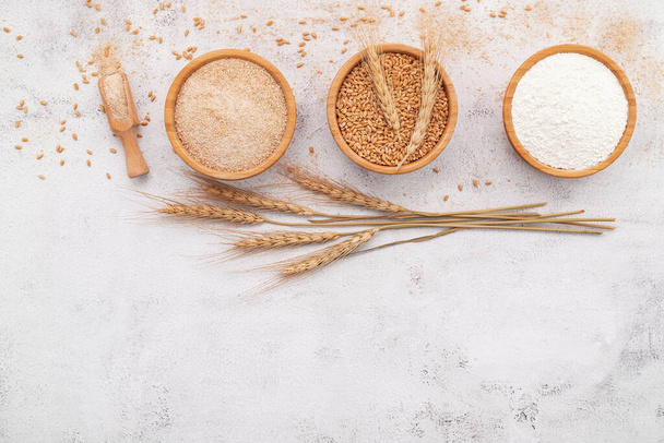 Пшеничные зерна, коричневая пшеничная мука и белая пшеничная мука в деревянной миске на белом бетонном фоне. - Фото, изображение