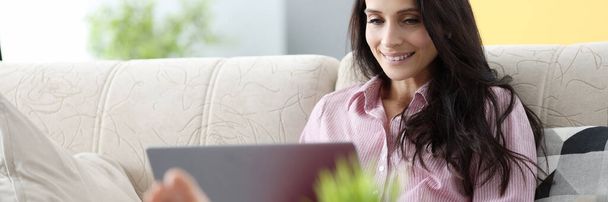 Woman is sitting on couch and working on laptop - Photo, image