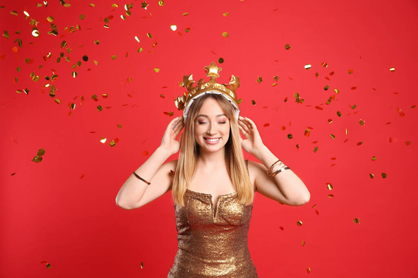 Happy young woman in party crown and confetti on red background - Zdjęcie, obraz