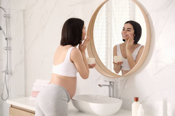 Young pregnant woman with cosmetic product in bathroom - Foto, Imagen