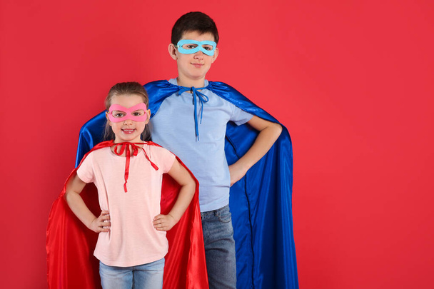 Boy and little girl in superhero costumes on red background. Space for text - Valokuva, kuva