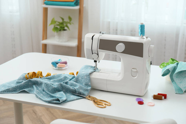Modern sewing machine, fabric and accessories on table indoors - Fotó, kép