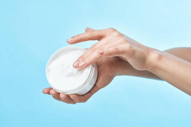 jar of cream in hand skin care close-up cosmetics blue background - Foto, afbeelding