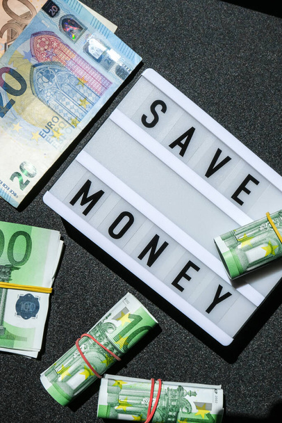 単語のLightboxボードユーロ紙幣の周りの黒い文字でお金を保存します。お金、ビジネス、金融、投資、貯蓄。現金請求書。富と繁栄の財政の事業予算。受動的所得 - 写真・画像