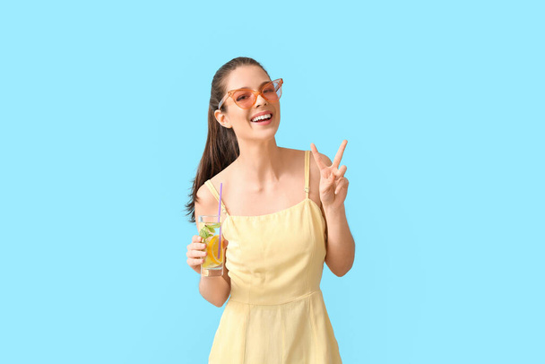 Молодая женщина со свежим лимонадом показывает победный жест на цветном фоне - Фото, изображение