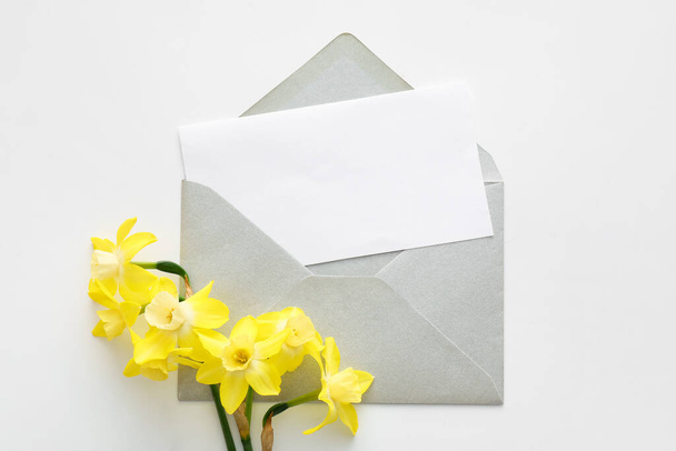 Красивые нарциссы и конверт с чистой карточкой на белом фоне - Фото, изображение
