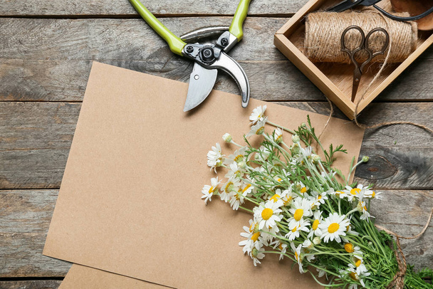 Kompozycja z pięknymi kwiatami rumianku, nożyczkami i kartką papieru na drewnianym tle - Zdjęcie, obraz