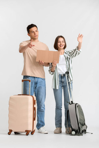 Young couple with cardboard and suitcases hitchhiking on light background - Foto, immagini