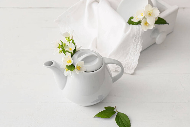 Composition with teapot and beautiful jasmine flowers on light background - Photo, Image