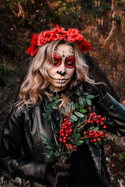 Calavera Catrina közeli portréja. Fiatal nő, cukorkoponyás sminkkel és vörös virágokkal. Dia de los muertos vagyok. A holtak napja. Halloweeni. - Fotó, kép