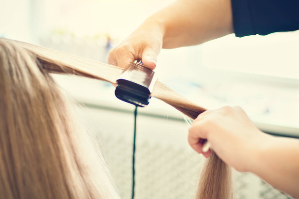 The hairdresser dries and combs a long fair hair. Hairdressing salon. - Valokuva, kuva