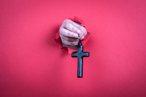 Croix en bois avec un cordon en cuir dans une main de femme sur un fond de papier rouge - Photo, image
