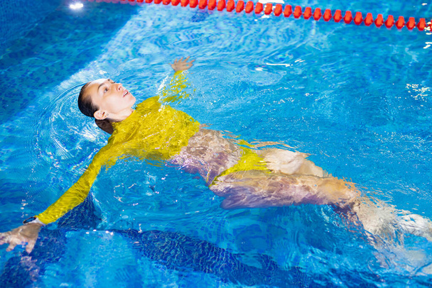 Woman swims on her back in interior pool - Foto, Bild
