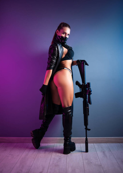 sexy Killer in Unterwäsche und Lederregenmantel und langen Lederschuhen mit einem m16 Automatikgewehr mit Zielfernrohr - Foto, Bild