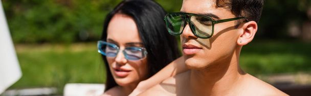Hombre en gafas de sol de pie cerca borrosa novia al aire libre, pancarta  - Foto, Imagen