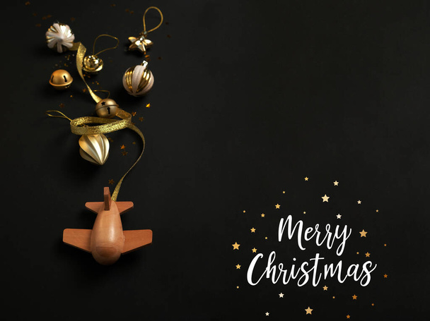 wooden children's plane with different christmas gold decoration on a black background. Merry christmas concept. Airplane lucky new year. Holiday comes to us - Фото, зображення