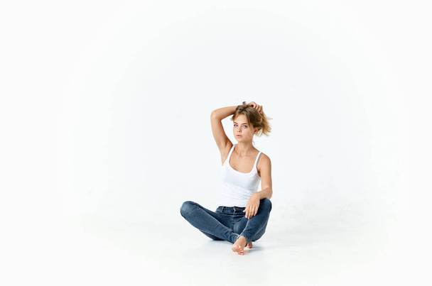 woman in white t-shirt and jeans sits on the floor holding her hair - Foto, Imagen