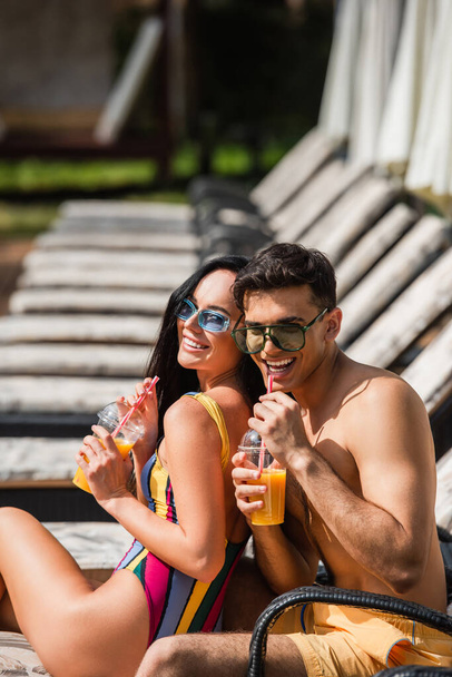 Smiling couple in swimwear drinking orange juice on deck chair  - Photo, Image