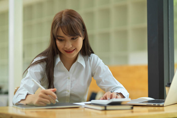 Estudiante universitaria haciendo deberes y dando conferencias en tableta en la biblioteca - Foto, Imagen