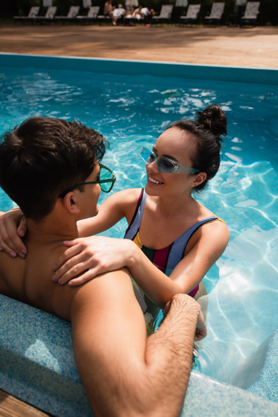 Happy girlfriend embracing man in sunglasses in swimming pool  - Foto, afbeelding