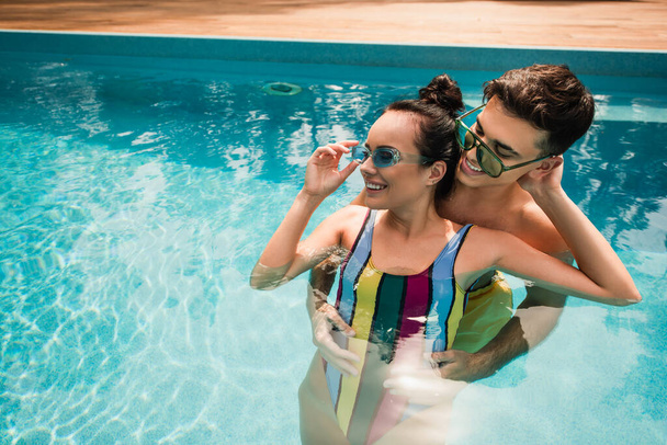 Smiling man hugging cheerful girlfriend in swimsuit in swimming pool  - Foto, Imagem