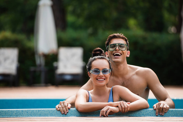 Homme torse nu debout près de la petite amie dans la piscine pendant les vacances  - Photo, image