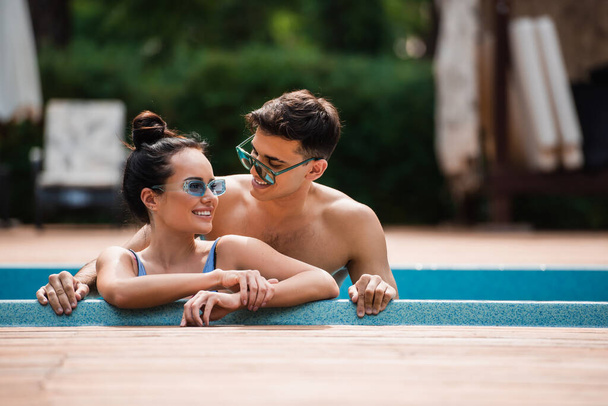 Glimlachende man kijkt naar vriendin in zwembad op resort  - Foto, afbeelding