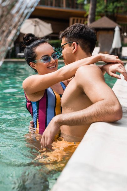 Hübsche Frau umarmt Freund in der Nähe von verschwommenem Pool  - Foto, Bild