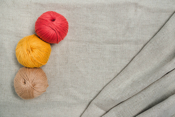 グレーのリネン生地に糸、赤、黄色、ベージュの3つのハンク。編み物、刺繍、かぎ針編み、パンチの仕事. - 写真・画像