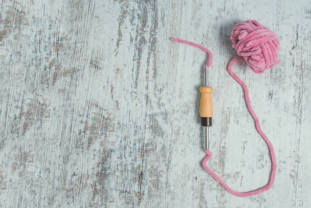 Punch naald met roze velours draad passeerde door en een bal van deze draad het op een achtergrond van shabby wit hout. Borduurwerk met naalden. - Foto, afbeelding