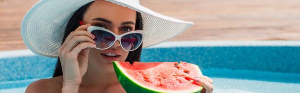Fiatal nő kezében napszemüveg és görögdinnye közelében elmosódott medence, banner  - Fotó, kép