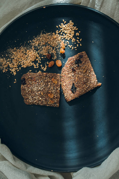 Vue de dessus de deux pains de lin avec des raisins secs sur une assiette noire. Deux rayons de lumière touchent légèrement la surface. - Photo, image