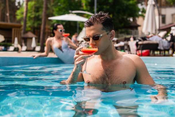 Giovane uomo che beve cocktail in piscina sul resort  - Foto, immagini