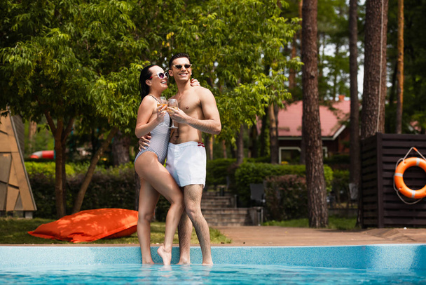Happy couple holding glasses of wine near pool during vacation  - Foto, imagen