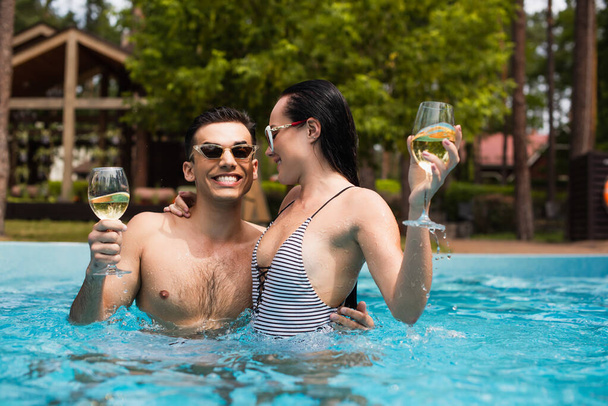 Woman hugging happy boyfriend with wine in swimming pool  - Fotó, kép